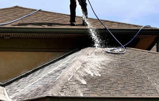 Professional roof cleaning in action with water spraying on shingles